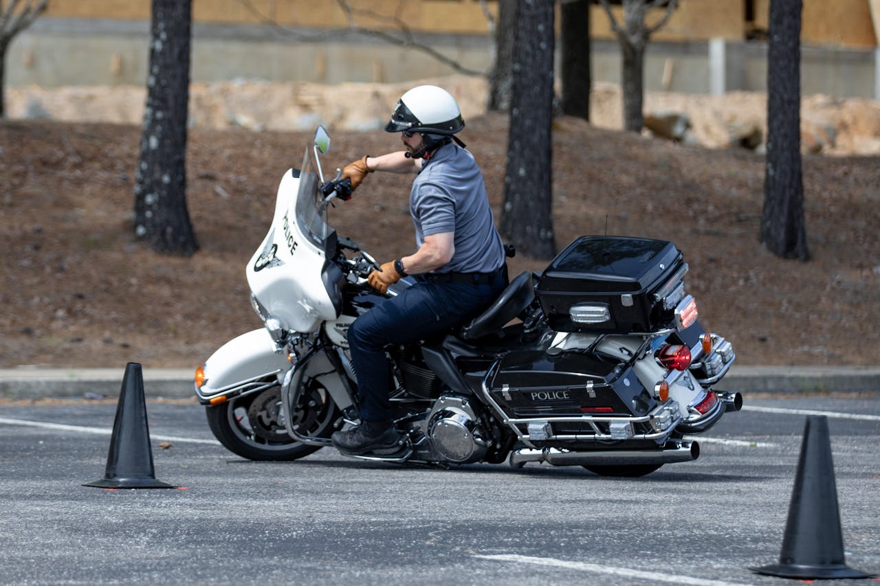 Police officer on a motorcycle practicing maneuvers between traffic cones outdoors.